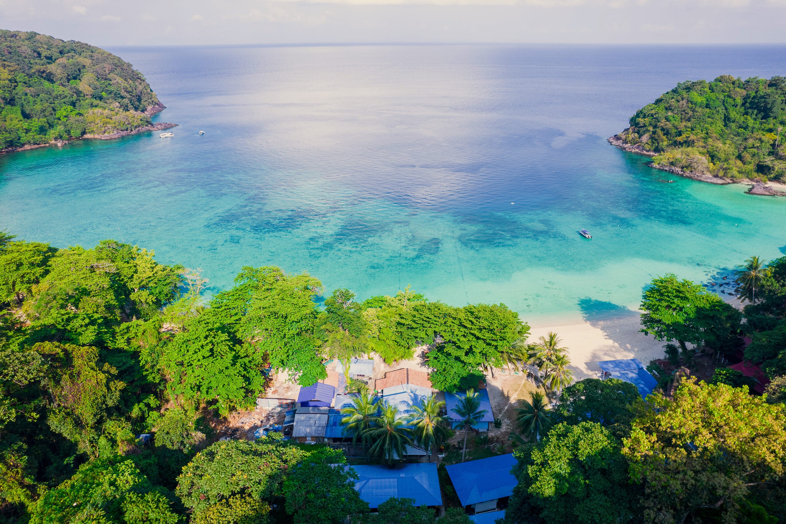 Wide drone aerial of the full Tenggol bay showing white sand beach, turquoise water, and resort buildings